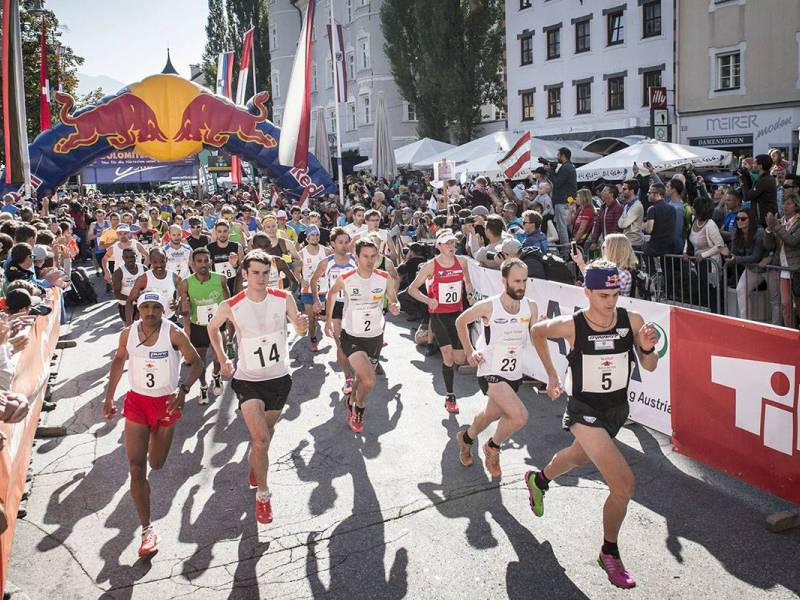 Eine Gruppe von Läufern startet ein Rennen vor einer jubelnden Menge unter einem Red Bull-Banner.