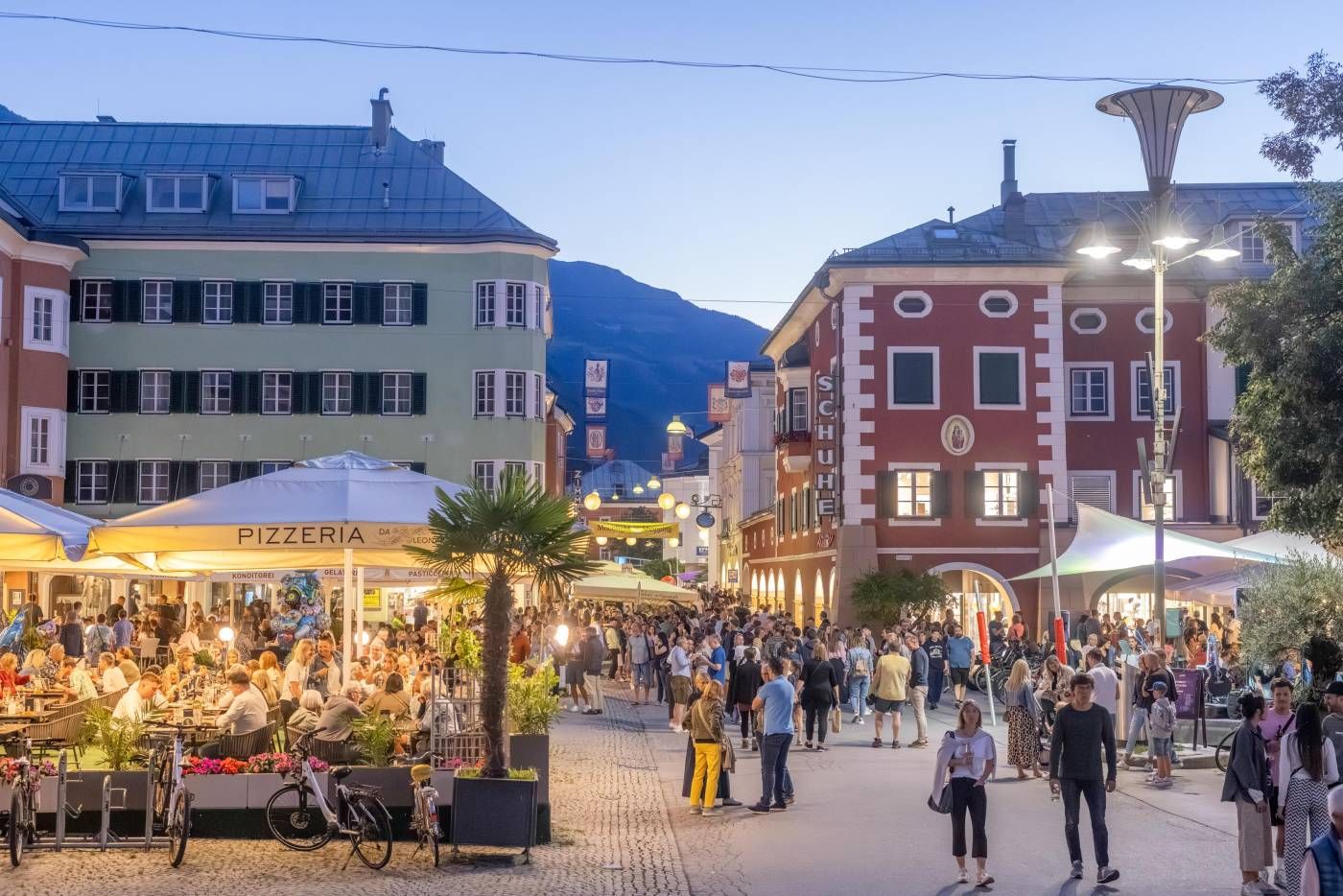 Belebte Straße mit Cafés und Restaurants bei Abenddämmerung, Menschen genießen das Leben in einer malerischen Stadt.