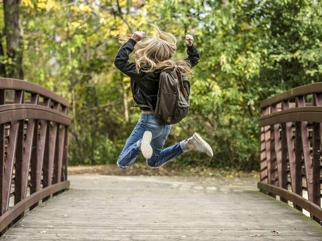 Ein Kind springt fröhlich über eine Holzbrücke in einem grünen Park. Herbstfarben umgeben die Szene.