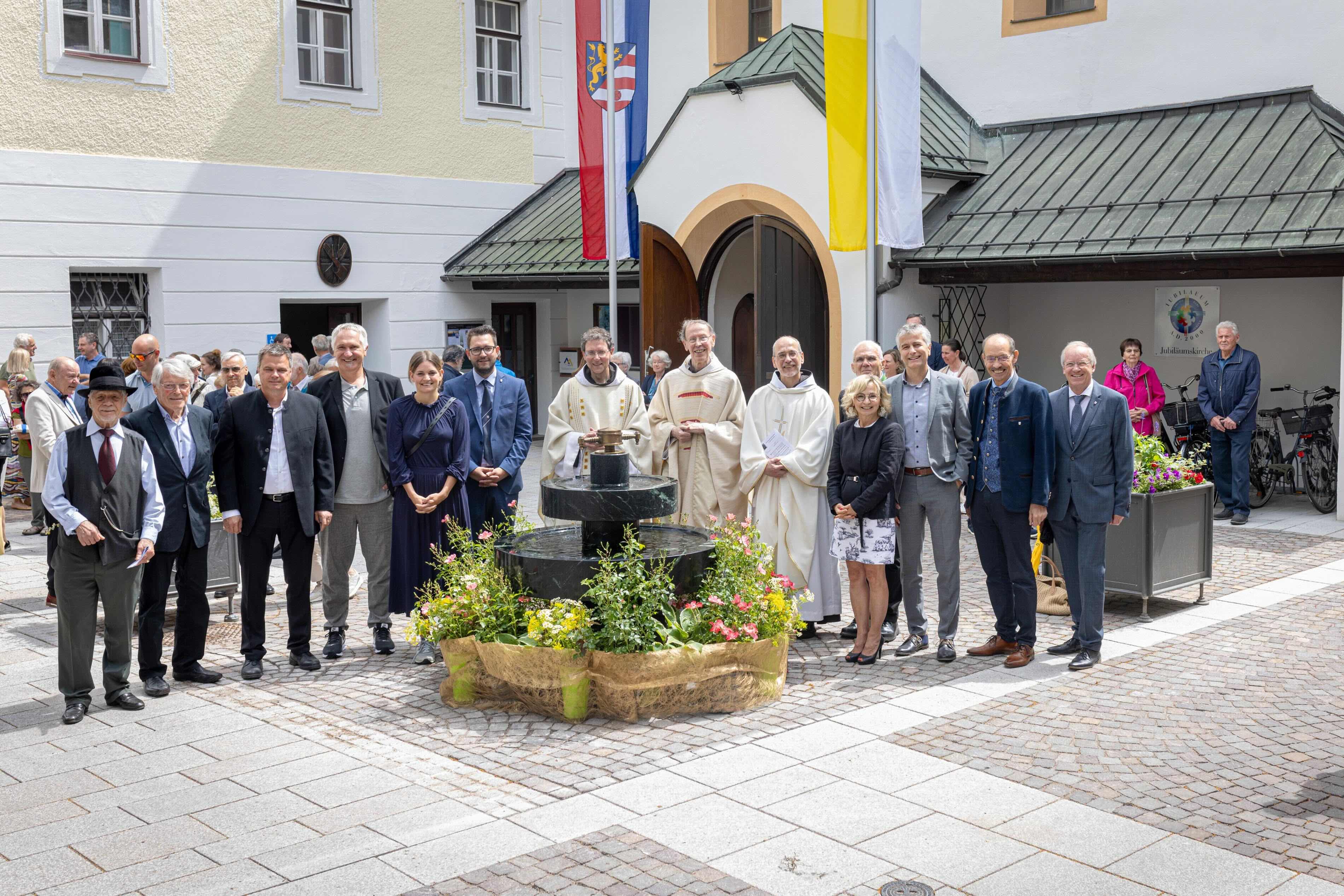 Gruppierung von Personen in einem Innenhof, mit einem Brunnen und Blumen, festliche Atmosphäre.