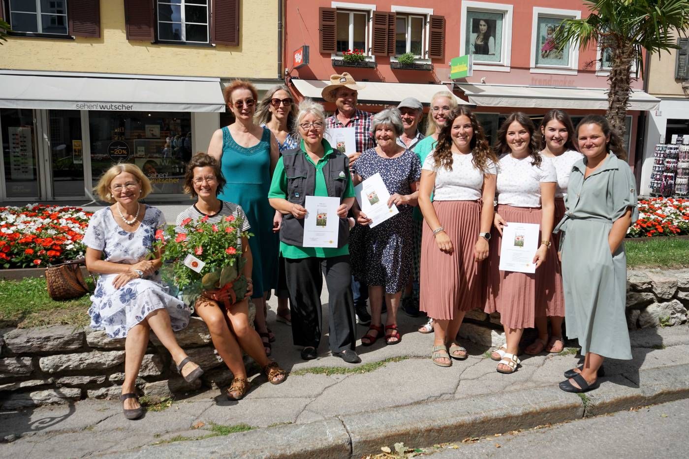 Eine Gruppe Frauen posiert draußen, umgeben von Blumen, mit Urkunden in der Hand und lächelnd in die Kamera.