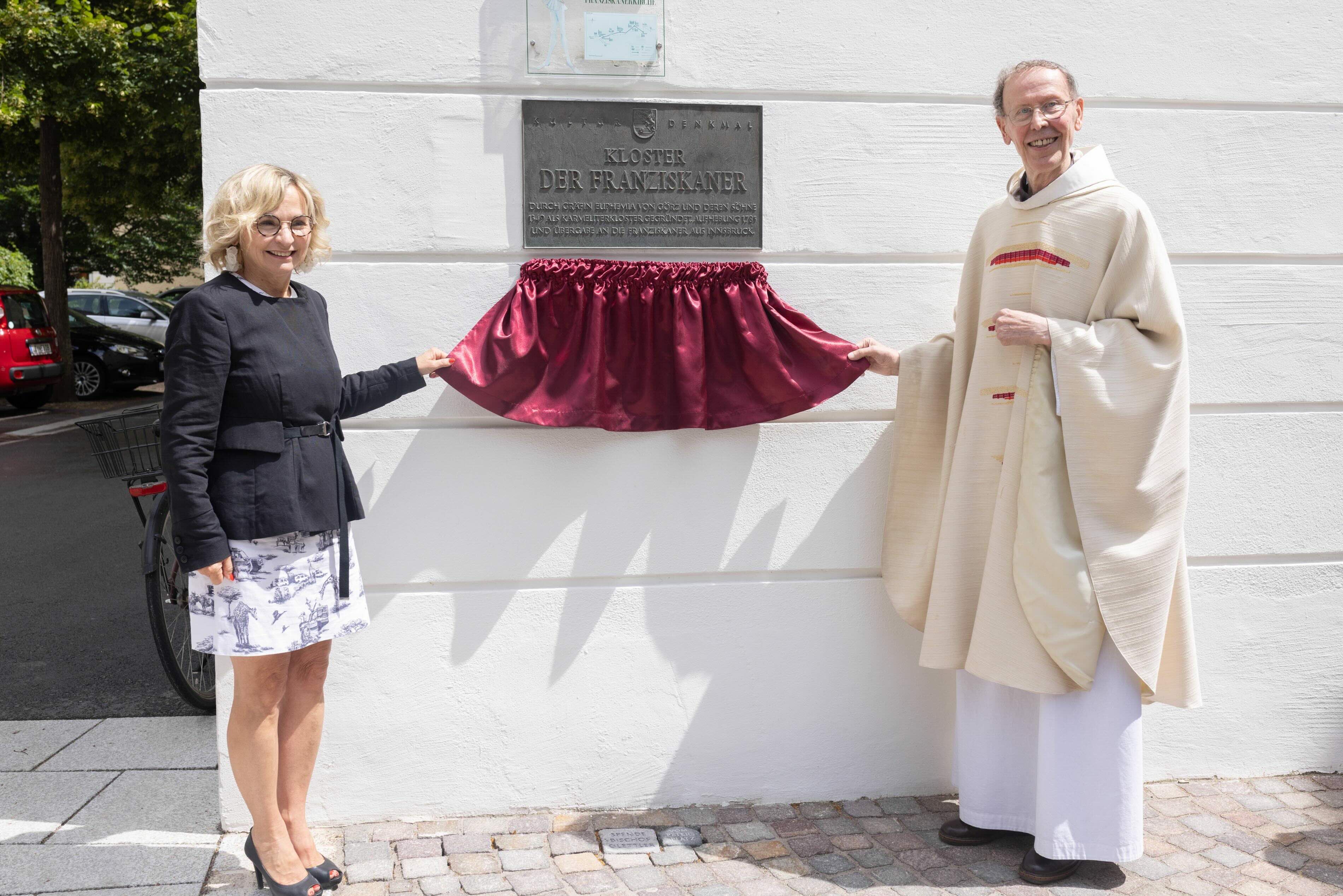 Ein Festakt zur Enthüllung einer Gedenktafel am Kloster der Franziskaner mit zwei lächelnden Personen.