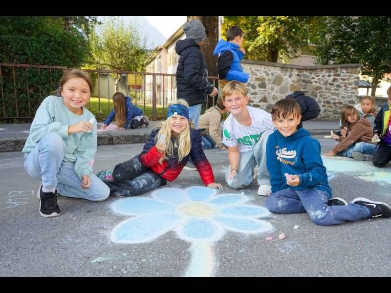 Kinder zeichnen mit Kreide einen großen Blumenentwurf auf der Straße und haben viel Spaß dabei.