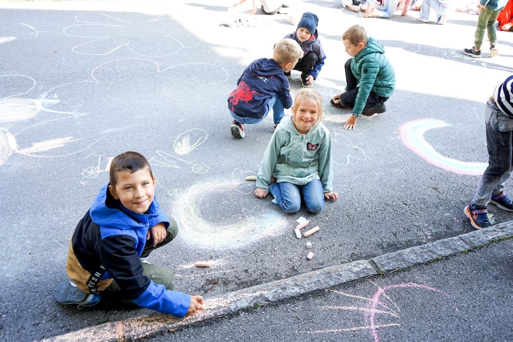 Kinder zeichnen mit Kreide auf dem Gehweg, lachen und haben Spaß an einem sonnigen Tag.