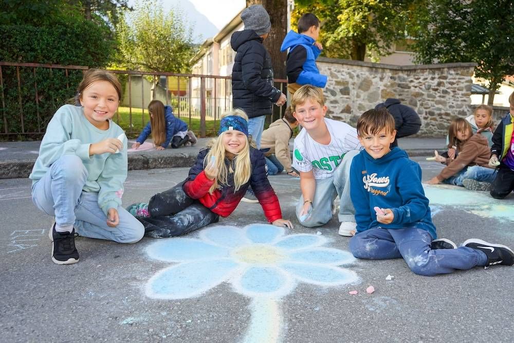 Kinder zeichnen mit Kreide einen großen Blumenentwurf auf der Straße und haben viel Spaß dabei.