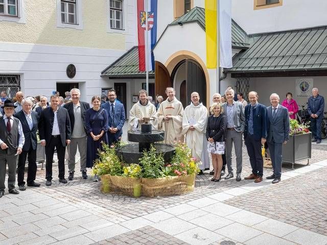 Eine Gruppe von Personen posiert vor einem Gebäude mit Blumen und Flaggen, wahrscheinlich bei einer Feierlichkeit.