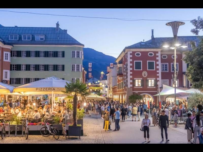 Belebte Straße mit Cafés und Restaurants bei Abenddämmerung, Menschen genießen das Leben in einer malerischen Stadt.