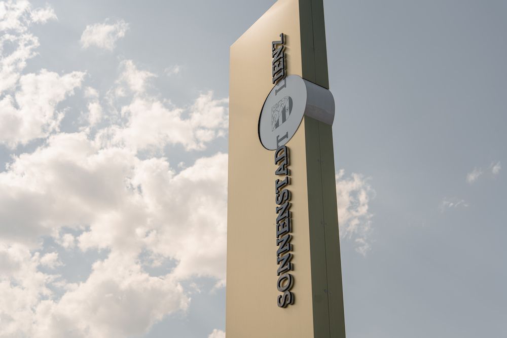 Großes, modern gestaltetes Werbeschild mit der Aufschrift 'SONNENSTADT LIENZ', das in den Himmel ragt. Der Himmel ist teils bewölkt mit blauem Hintergrund.