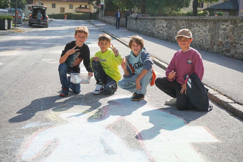 Vier Kinder posieren fröhlich auf einer Straße, umgeben von farbiger Kreidekunst und einer entspannten Atmosphäre.