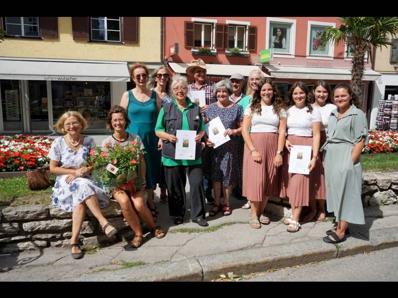 Eine Gruppe Frauen posiert draußen, umgeben von Blumen, mit Urkunden in der Hand und lächelnd in die Kamera.